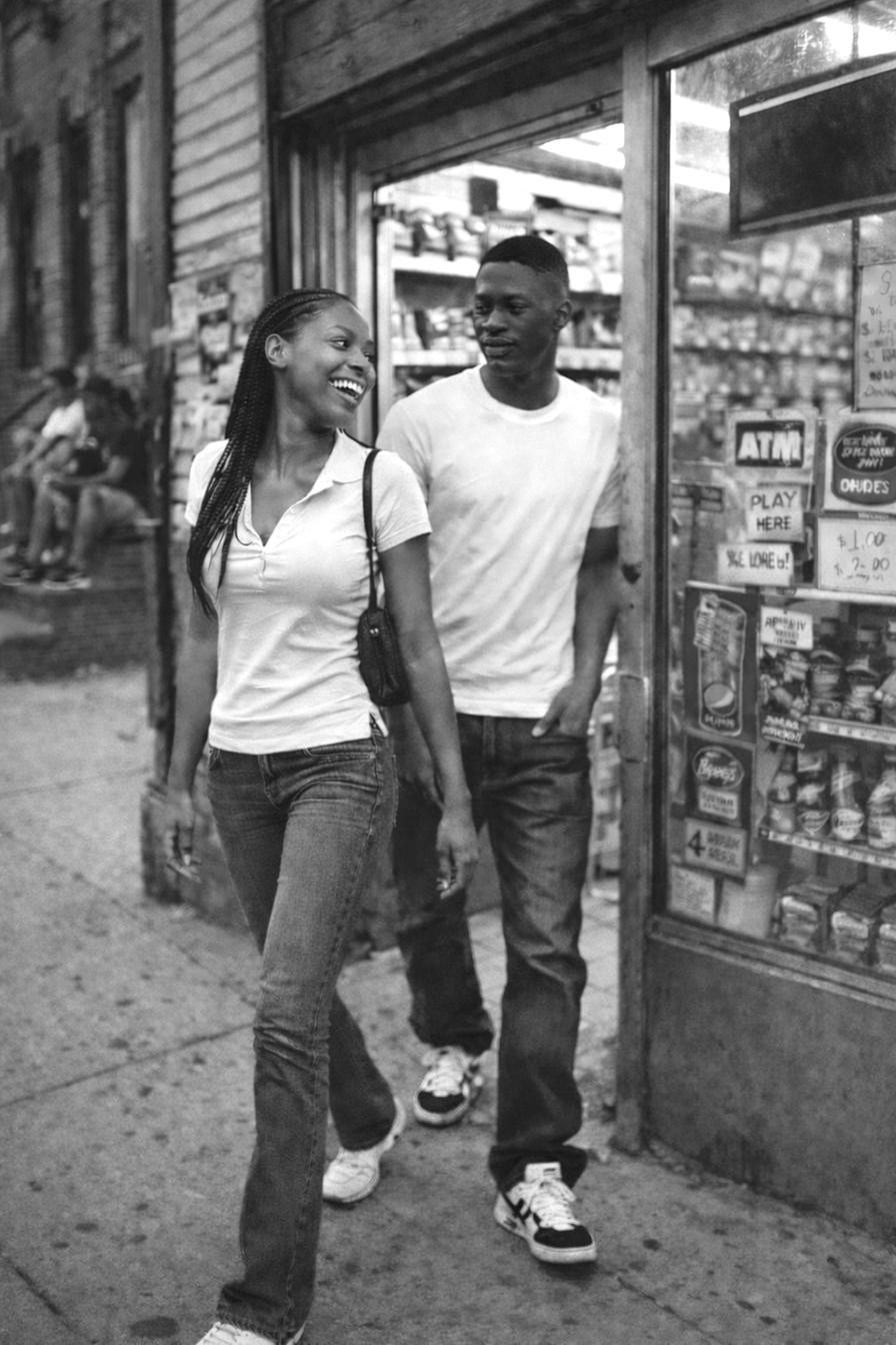 Two people walking past a corner store covered in flyers.